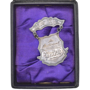 An antique silver-plated "Quarter-Final" award medal with an engraved shield and ribbon bar, displayed inside a dark presentation box lined with purple satin.